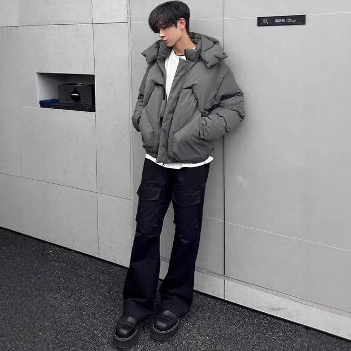 Person wearing a gray puffer jacket and black pants against a gray wall.