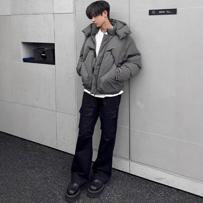 Person wearing a gray puffer jacket and black pants against a gray wall.