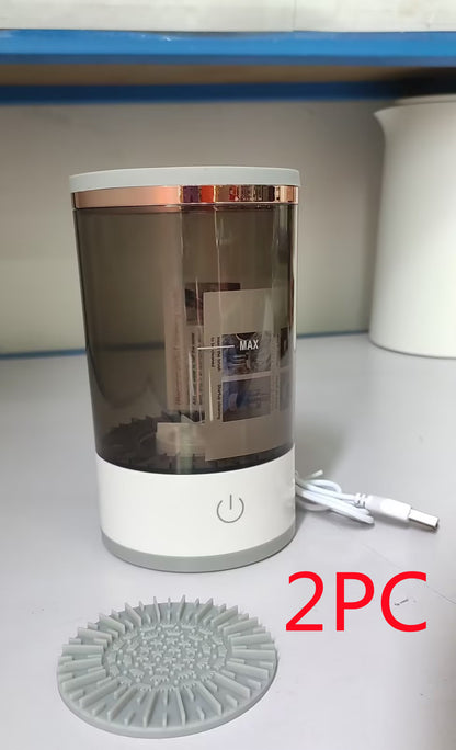 Transparent cylindrical container with rose gold accents on a white surface, accompanied by a gray silicone mat and white cable.