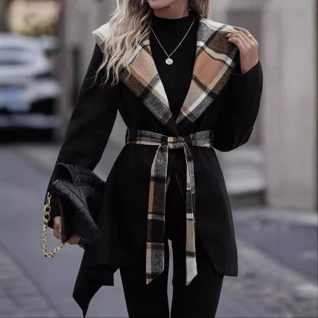 Person wearing a black coat with plaid scarf and belt, holding a black clutch on a blurred street background