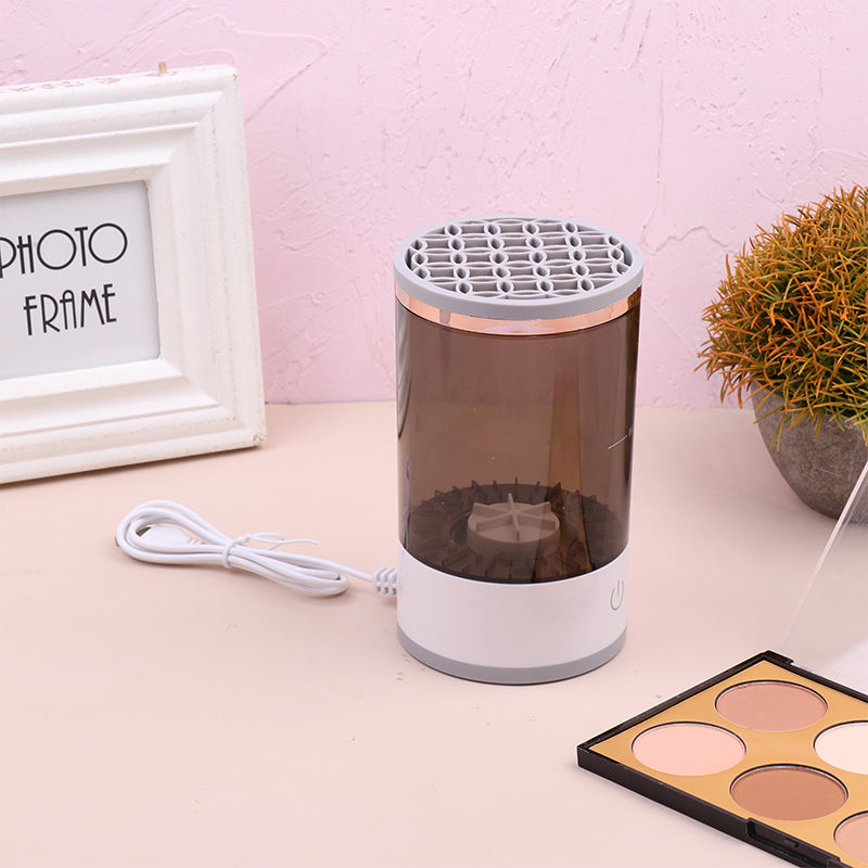 Small cylindrical device with a white base and gray top on a pink surface with a photo frame and plant in the background.