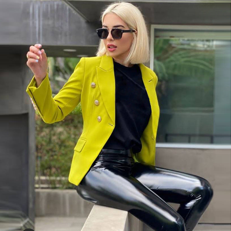 Woman wearing a bright yellow blazer and black pants sitting outdoors.