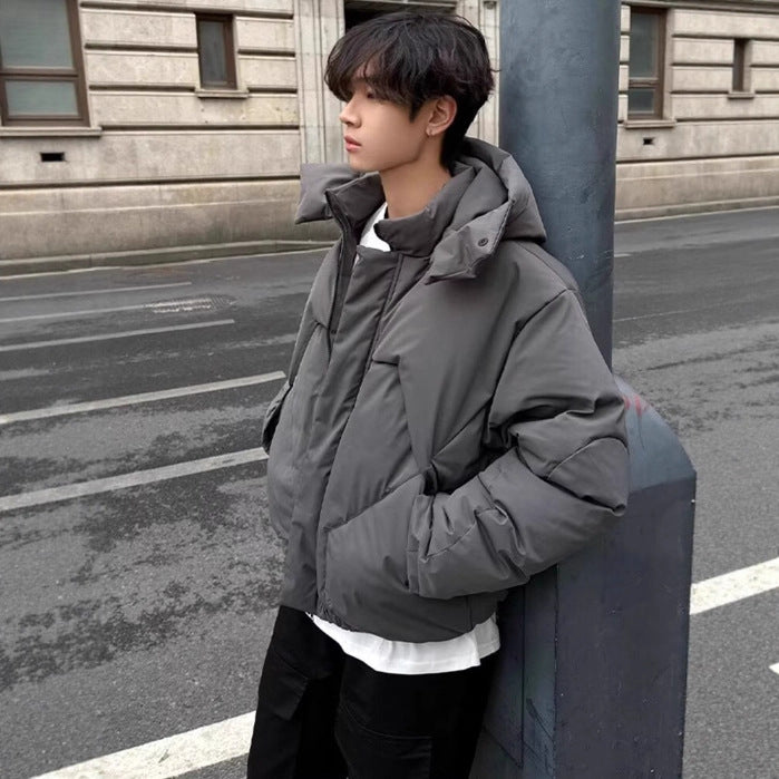 Person wearing a gray jacket leaning against a pole on a street.